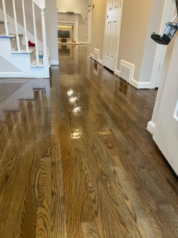 Glossy refinished oak hardwood floor running down a hallway beside a staircase