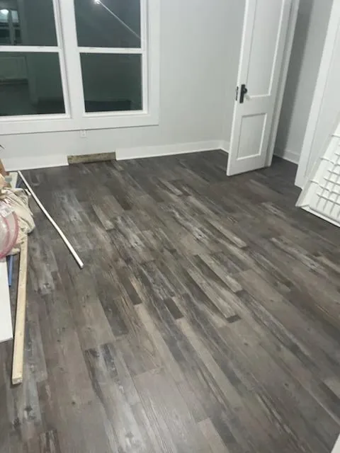 Charcoal gray plank flooring in a bright room with a white door and windows
