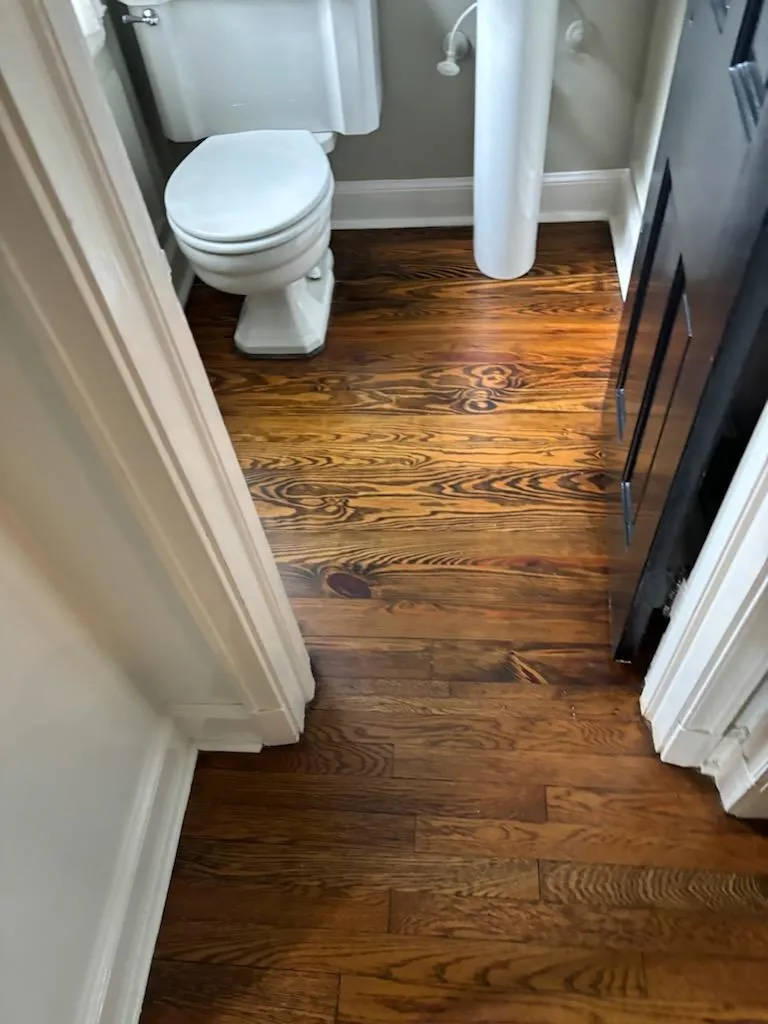 Stained and sealed hardwood floor in a small bathroom with a white pedestal sink